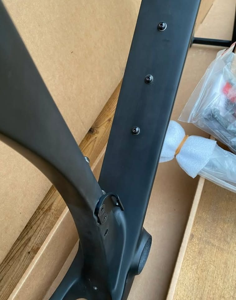 Unpainted black carbon 3T frame and fork standing in front of the 3T cardboard box they came in, with a wrapped seatpost and two sealed bags of hardware on the boards in front, from the seller's Marketplace listing. Photo 2 of 4.