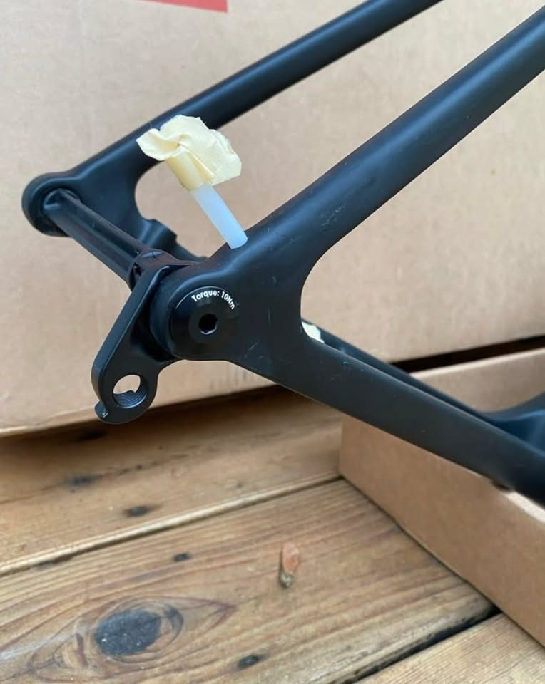 Unpainted black carbon 3T frame and fork standing in front of the 3T cardboard box they came in, with a wrapped seatpost and two sealed bags of hardware on the boards in front, from the seller's Marketplace listing. Photo 3 of 4.