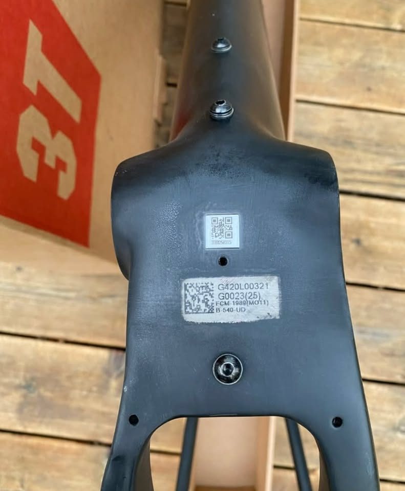 Unpainted black carbon 3T frame and fork standing in front of the 3T cardboard box they came in, with a wrapped seatpost and two sealed bags of hardware on the boards in front, from the seller's Marketplace listing. Photo 4 of 4.