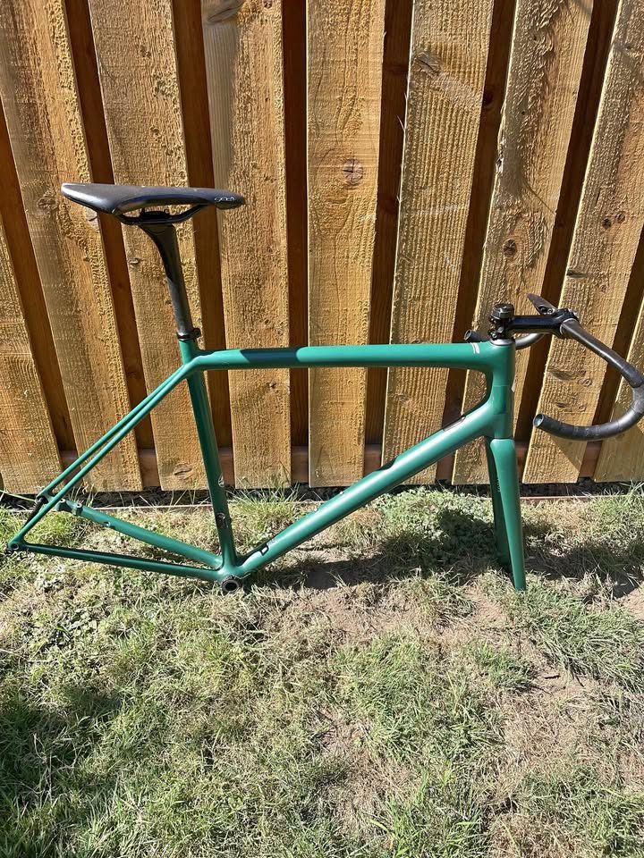 Green Specialized Aethos frameset leaning against a fence with its fork, seatpost and saddle fitted, from the seller's Marketplace listing.