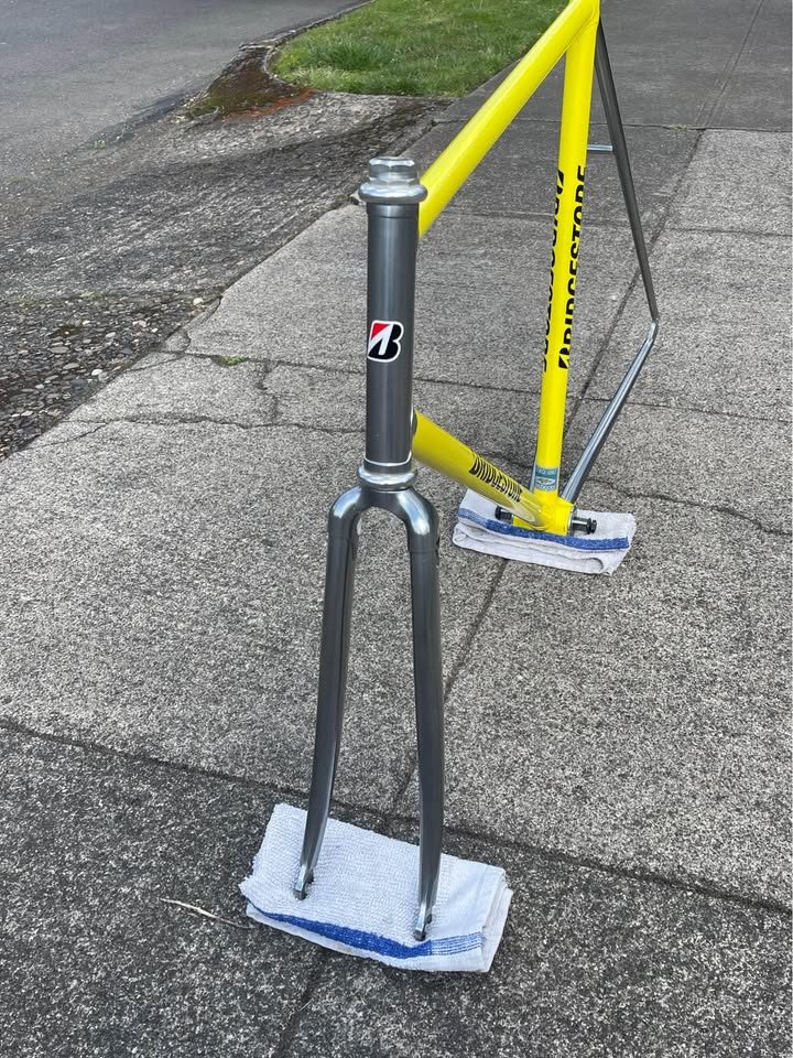 Yellow Bridgestone track frame with a polished silver rear triangle propped on a pavement beside its matching silver fork, from the seller's Marketplace listing. Photo 2 of 5.