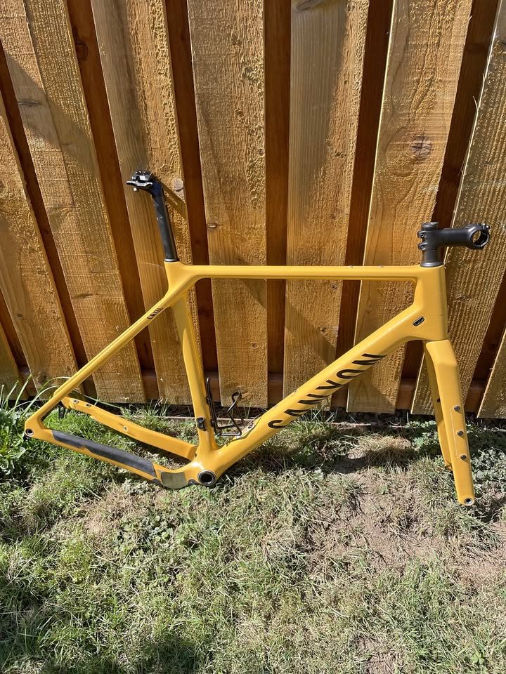 Mustard yellow Canyon Grizl carbon frameset leaning against a wooden fence with its fork, stem and seatpost alongside, from the seller's Marketplace listing.