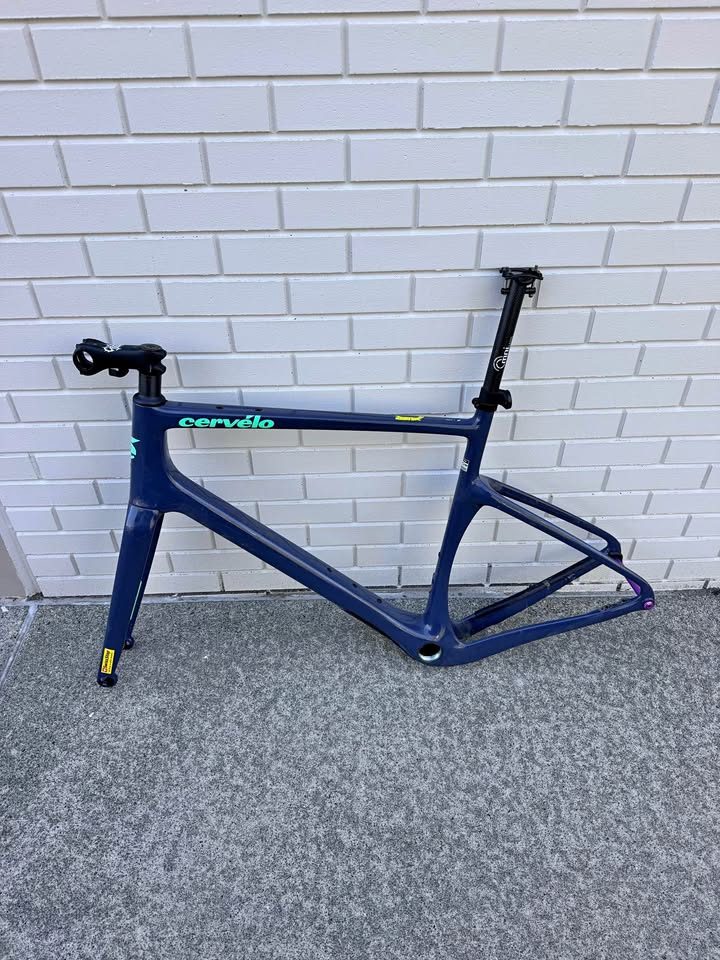 Dark blue Cervélo Áspero frame and fork with a stem and seatpost fitted and purple axles, leaning against a white brick wall, from the seller's Marketplace listing. Photo 2 of 9.