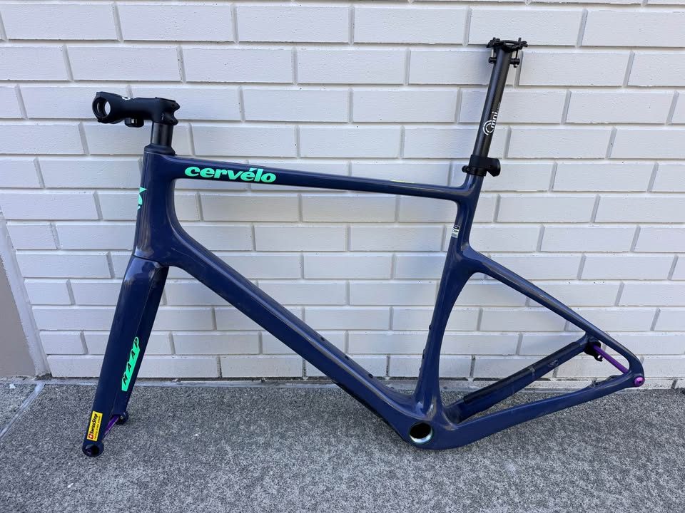 Dark blue Cervélo Áspero frame and fork with a stem and seatpost fitted and purple axles, leaning against a white brick wall, from the seller's Marketplace listing. Photo 3 of 9.