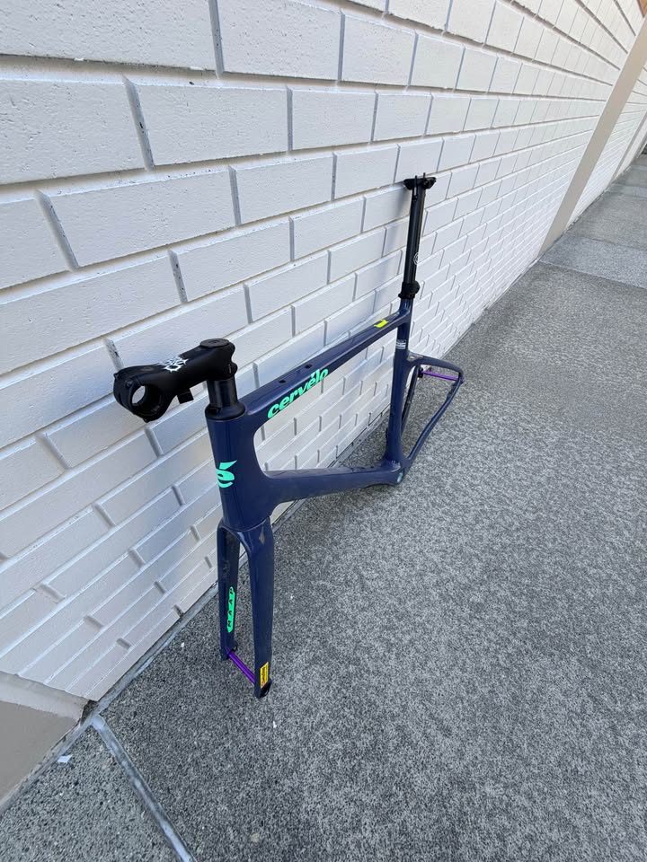 Dark blue Cervélo Áspero frame and fork with a stem and seatpost fitted and purple axles, leaning against a white brick wall, from the seller's Marketplace listing. Photo 4 of 9.