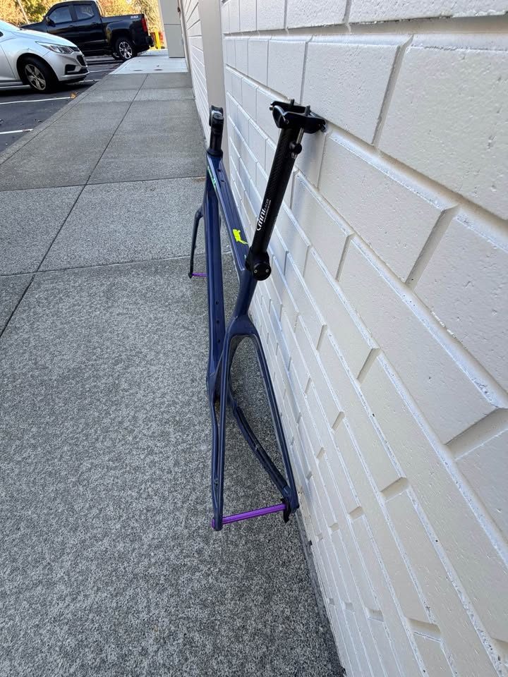Dark blue Cervélo Áspero frame and fork with a stem and seatpost fitted and purple axles, leaning against a white brick wall, from the seller's Marketplace listing. Photo 6 of 9.