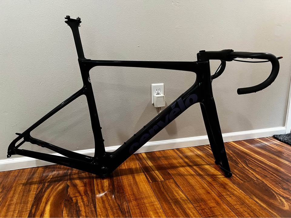 Black Cervélo Caledonia-5 frameset with the bar and stem fitted, leaning against a wall on a wood floor, from the seller's Marketplace listing.