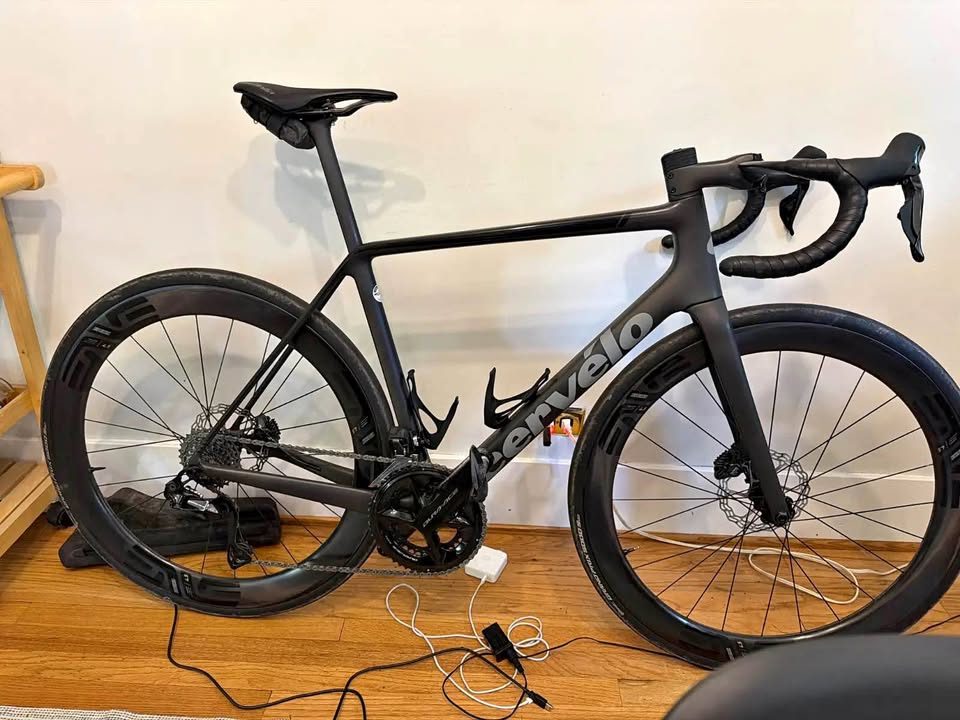 Black Cervélo R5 built up with drop bars and deep carbon wheels, leaning against a wall indoors, from the seller's Marketplace listing.