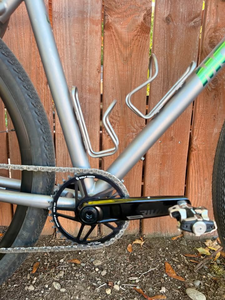 Titanium Moots Routt 45 built up as a complete bike with green Moots graphics, a black carbon fork and DT Swiss wheels, leaning against a wooden fence, from the seller's Marketplace listing. Photo 3 of 8.