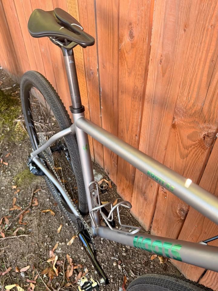 Titanium Moots Routt 45 built up as a complete bike with green Moots graphics, a black carbon fork and DT Swiss wheels, leaning against a wooden fence, from the seller's Marketplace listing. Photo 5 of 8.
