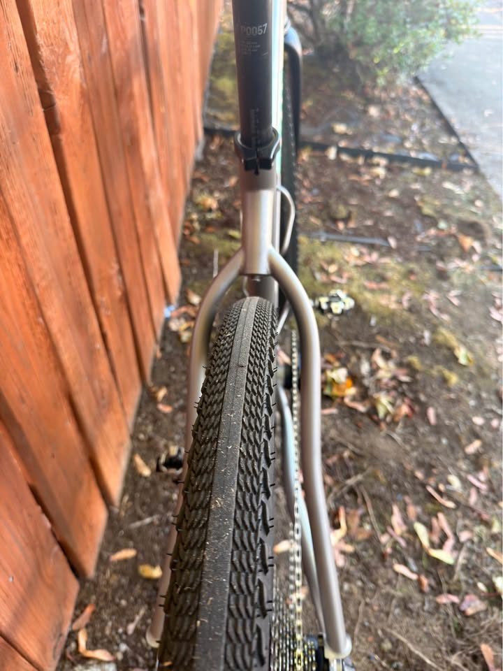Titanium Moots Routt 45 built up as a complete bike with green Moots graphics, a black carbon fork and DT Swiss wheels, leaning against a wooden fence, from the seller's Marketplace listing. Photo 7 of 8.