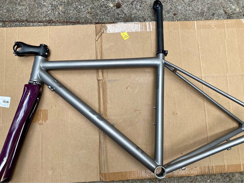 Brushed titanium Mosaic road frameset laid out on cardboard next to its purple carbon fork, from the seller's Marketplace listing.