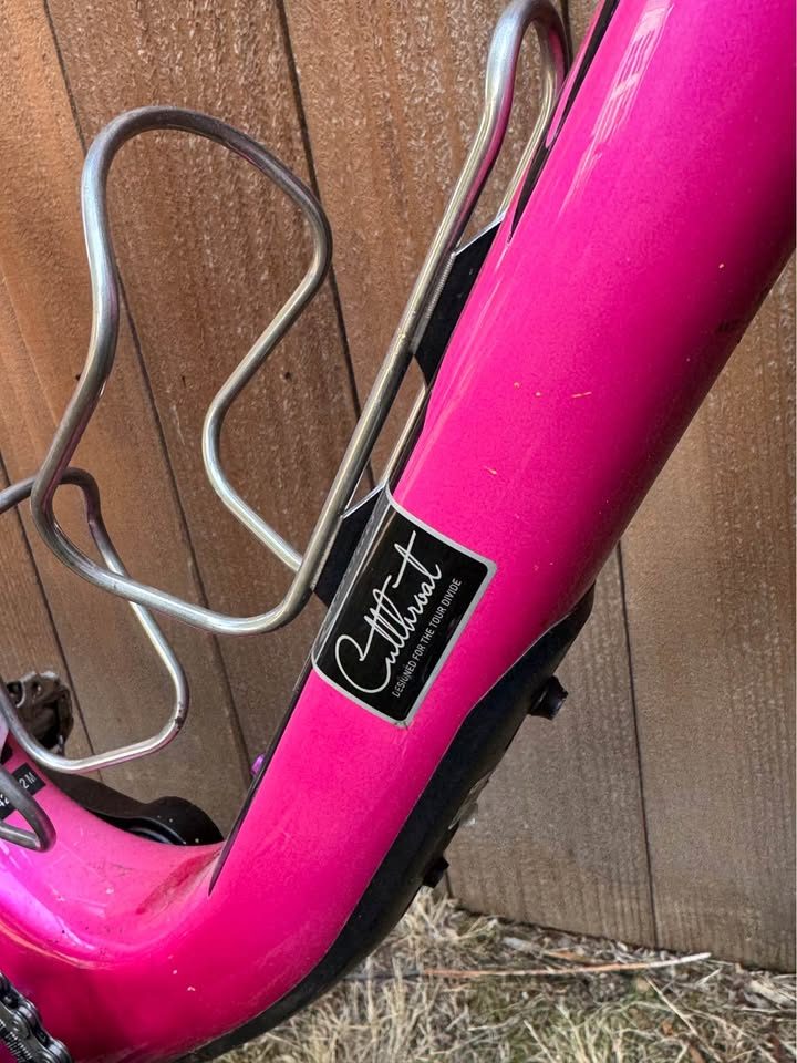 Hot pink Salsa Cutthroat leaning against a wood fence, built up with drop bars, tan wall knobby tyres and a frame bag and seat pack, from the seller's Marketplace listing. Photo 2 of 7.