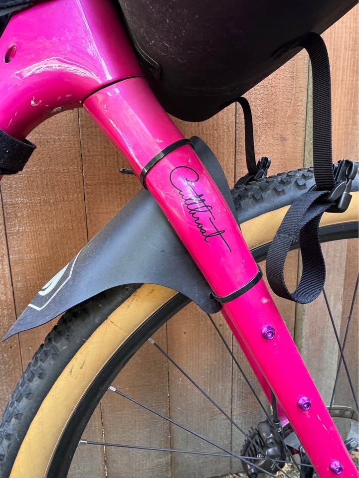 Hot pink Salsa Cutthroat leaning against a wood fence, built up with drop bars, tan wall knobby tyres and a frame bag and seat pack, from the seller's Marketplace listing. Photo 3 of 7.