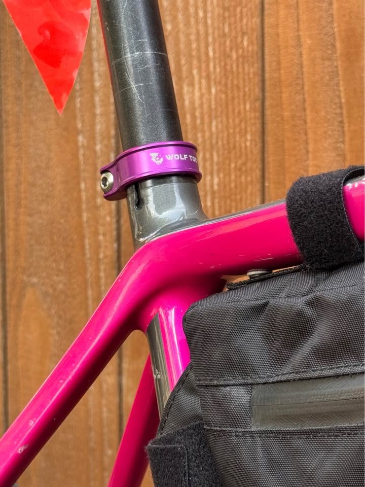 Hot pink Salsa Cutthroat leaning against a wood fence, built up with drop bars, tan wall knobby tyres and a frame bag and seat pack, from the seller's Marketplace listing. Photo 5 of 7.
