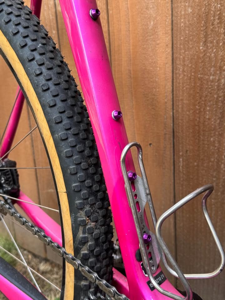 Hot pink Salsa Cutthroat leaning against a wood fence, built up with drop bars, tan wall knobby tyres and a frame bag and seat pack, from the seller's Marketplace listing. Photo 7 of 7.