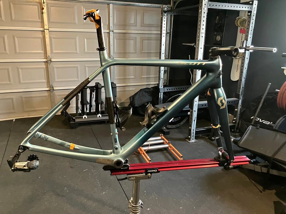 Blue-green Scott carbon frame and fork in a work stand in a garage, with a seatpost, stem and SRAM rear derailleur fitted, from the seller's Marketplace listing.