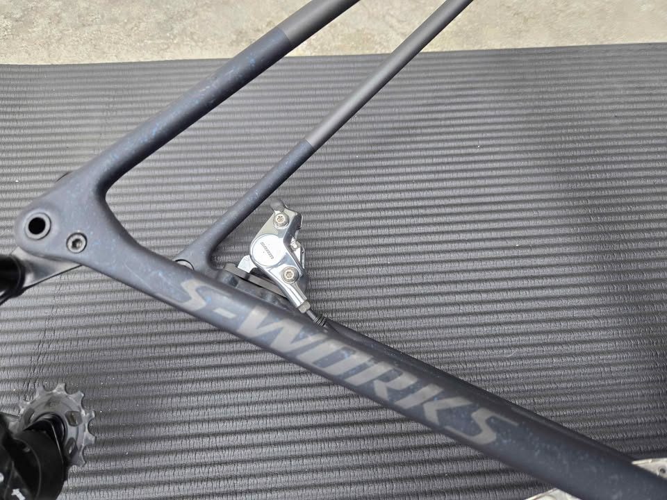 Rear triangle of a matte black S-Works Crux frame with blue speckles, a silver flat mount disc caliper bolted to the chainstay, from the seller's Marketplace listing.